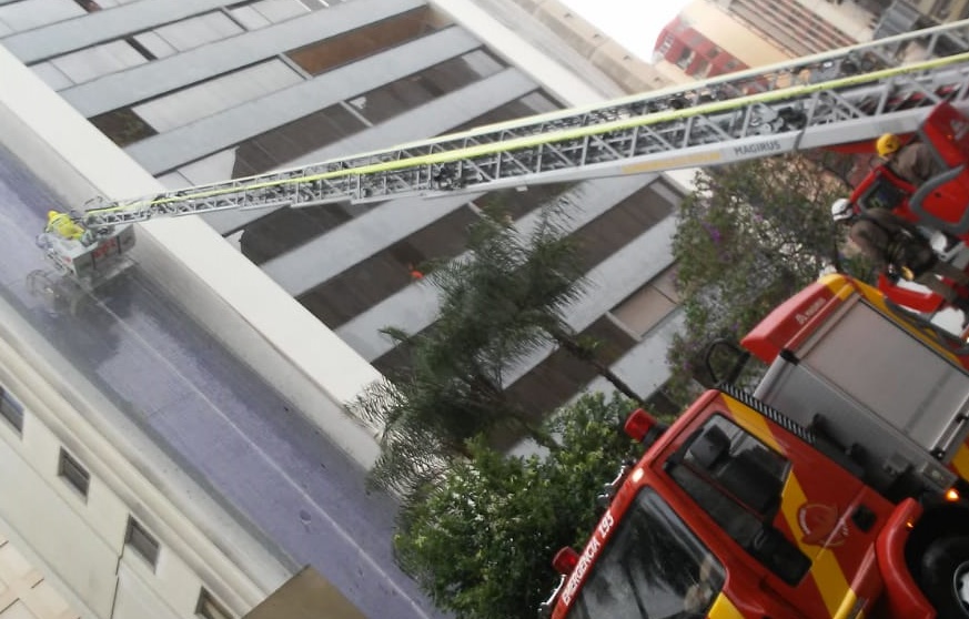 Corpo de bombeiros resgata homem que ficou preso do lado de fora do prédio durante chuva