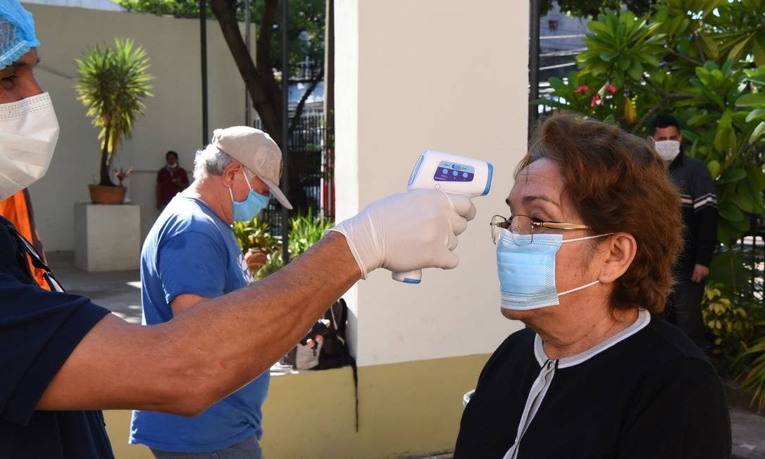 Profissional de saúde mede temperatura de idosa em Assunção, no Paraguai: país é um dos menos afetados na América Latina Foto: NORBERTO DUARTE / AFP