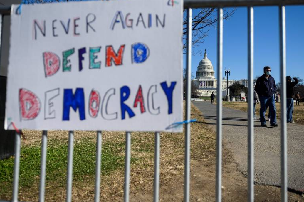 Cartaz com a frase “nunca outra vez, defenda a democracia” em grade que cerca o Capitólio (Foto: Andrew Caballero / AFP)