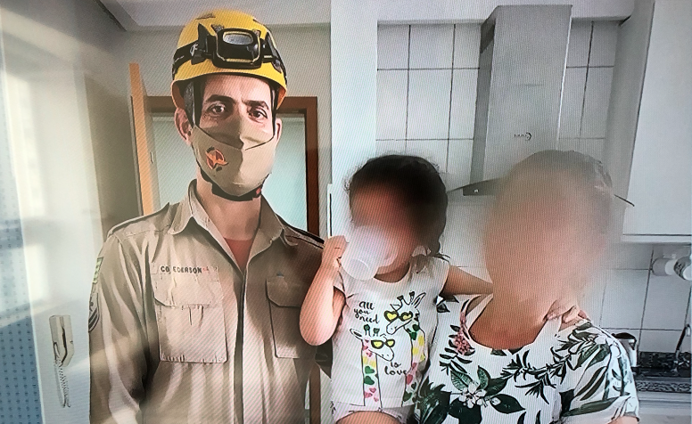 Bombeiro ao lado da criança que ele ajudou a resgatar e a mãe dela (Foto: Reprodução)