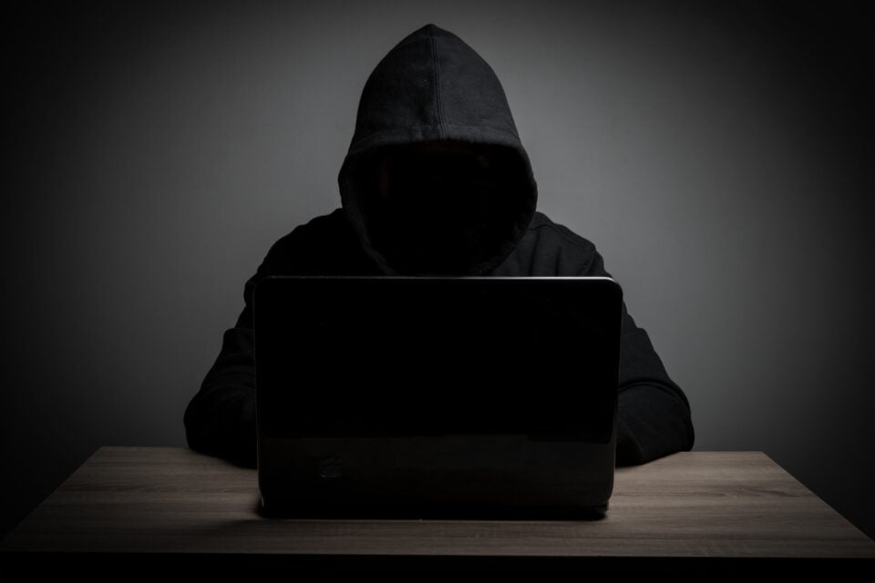 Hacker work front of his laptop computer with dark face.