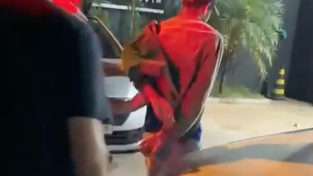 Imagem mostra suspeito sendo levado algemado para delegacia. Foto ilustra chamada: Jovem descumpre medida protetiva e ameaça mãe e irmã gestante em Jaraguá