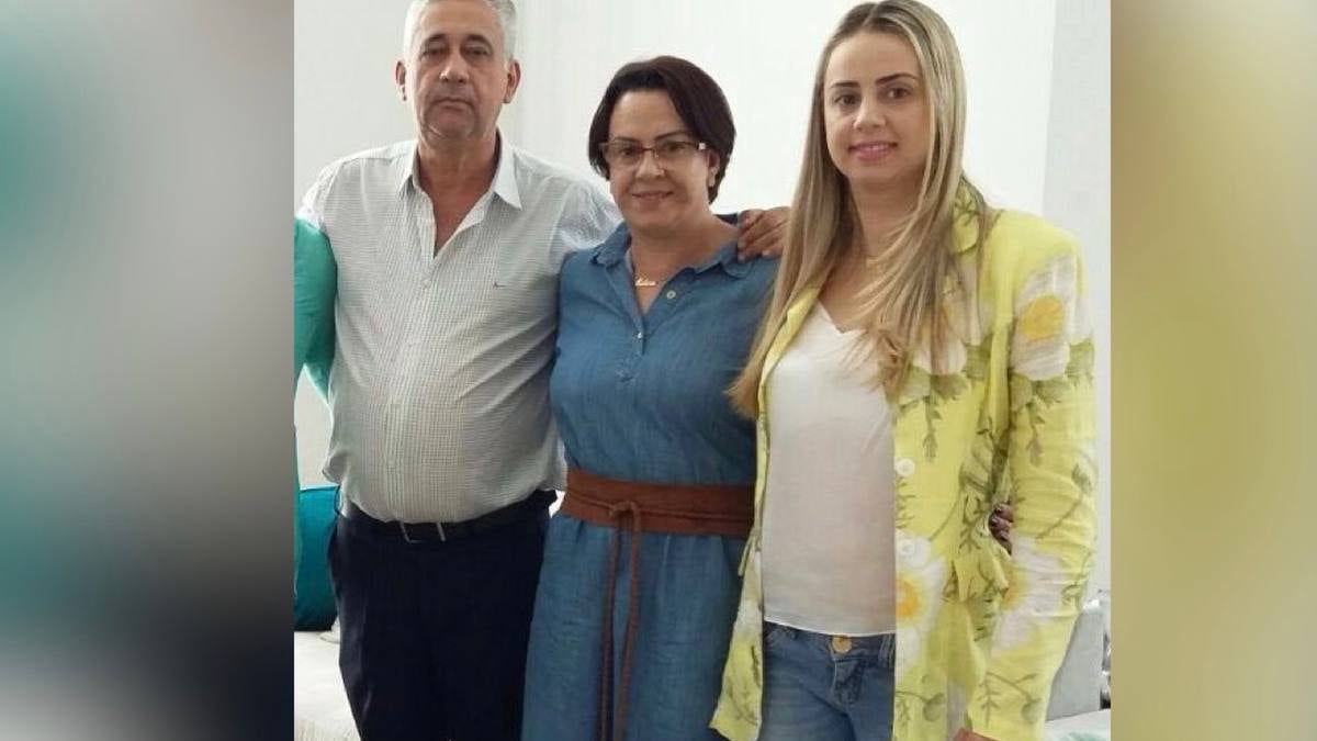 O pai à esquerda, a mãe no meio e a filha na outra extremidade posam para a foto. As duas mulheres sorriem e o homem se mantém sério.