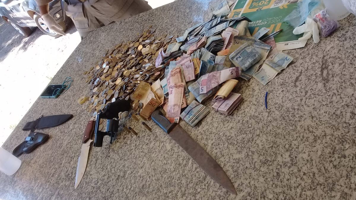 Grupo que pedia dinheiro com carros de som possuíam armas e facas dentro dos veículos. Imagem mostra mesa repleta de notas em papel e moedas, além das facas mencionadas