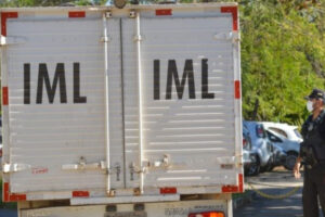 Foto mostra o fundo de um caminhão do IML. Há um agente civil ao lado. Foto ilustra chamada: Populares encontram corpo em decomposição com dois tiros em matagal próximo a GO-154