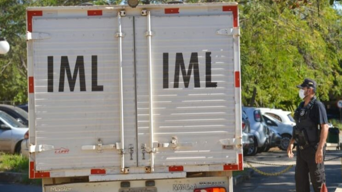 Foto mostra o fundo de um caminhão do IML. Há um agente civil ao lado. Foto ilustra chamada: Populares encontram corpo em decomposição com dois tiros em matagal próximo a GO-154