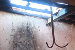 Imagem mostra teto descoberto e objeto metálico pendente. Na parede há vestígios de incêndio. Foto ilustra: Mulher tenta exterminar teias de aranha com maçarico e incendeia casa em Iporá