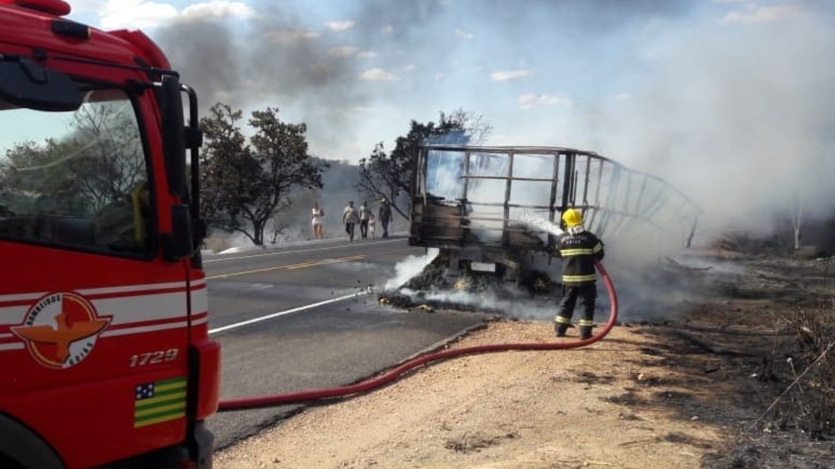 Bombeiro com mangueira de água tenta conter chamas em caminhão, que já está completamente carbonizado. Foto ilustra chamada: Incêndio destrói caminhão e carga após pane no motor na BR-414, em Niquelândia