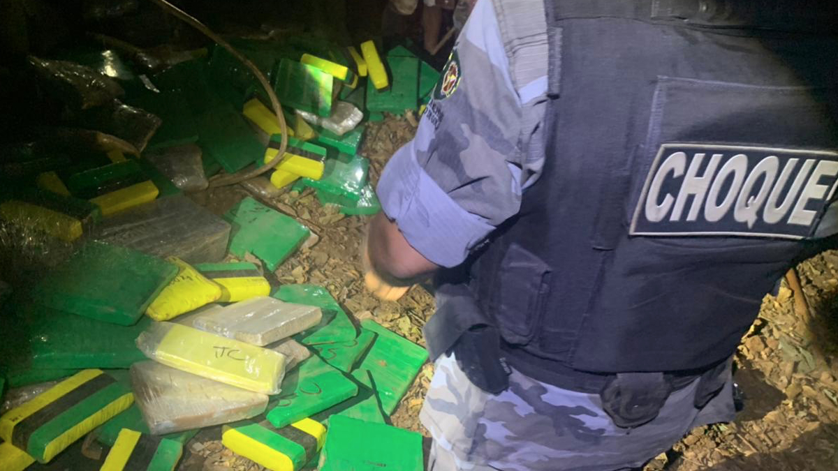 PM fardado com escrita "choque", referente ao batalhão. Homem está de costas e recolhe 1,5 toneladas de maconha de tonel.