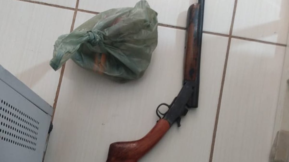 Espingarda encontrada entre os itens do fazendeiro. Arma está no chão ao lado de uma sacola