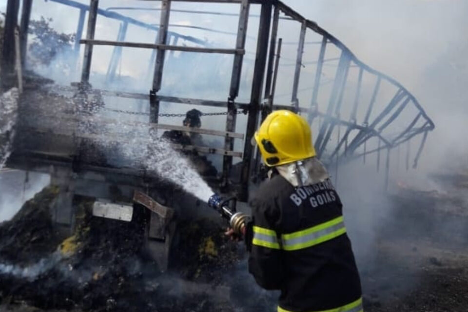 Bombeiro com mangueira de água tenta conter chamas em caminhão, que já está completamente carbonizado. Foto ilustra chamada: Incêndio destrói caminhão e carga após pane no motor na BR-414, em Niquelândia
