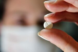 Pessoa segura comprimido - Anvisa aprova remédio de artrite e dermatite para tratamento de casos graves de Covid-19. Pacientes tem que usar máscara para respiração