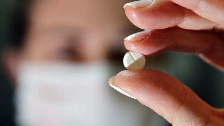 Pessoa segura comprimido - Anvisa aprova remédio de artrite e dermatite para tratamento de casos graves de Covid-19. Pacientes tem que usar máscara para respiração