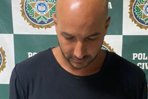 Homem calvo detido olha para baixo - Suspeito de comandar golpes contra idosos dava aulas de futevôlei em praia do RJ. Vítimas tiveram mais de R$ 1 milhão de prejuízo, segundo PC