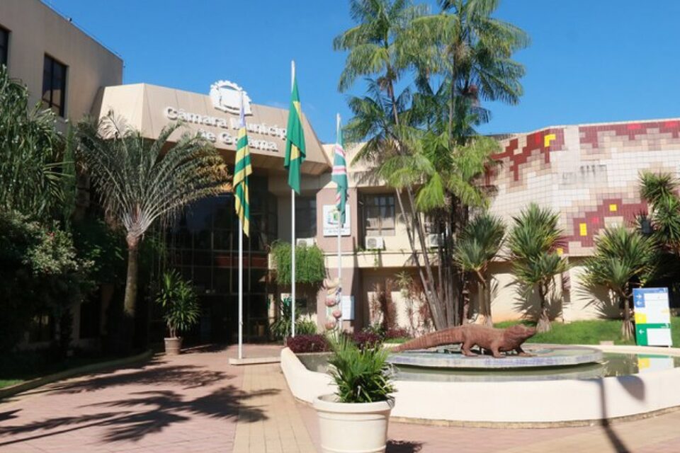 Entrada da Câmara Municipal de Goiânia com fonte e jacaré no primeiro plano e bandeiras no segundo