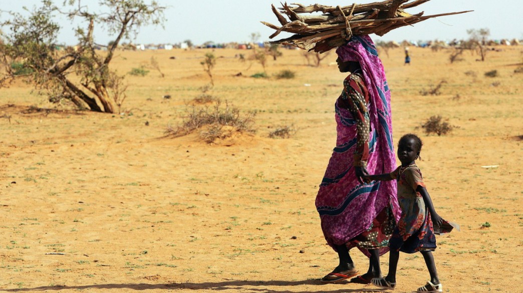 Mulher e criança africana passam com madeira debaixo de um forte sol