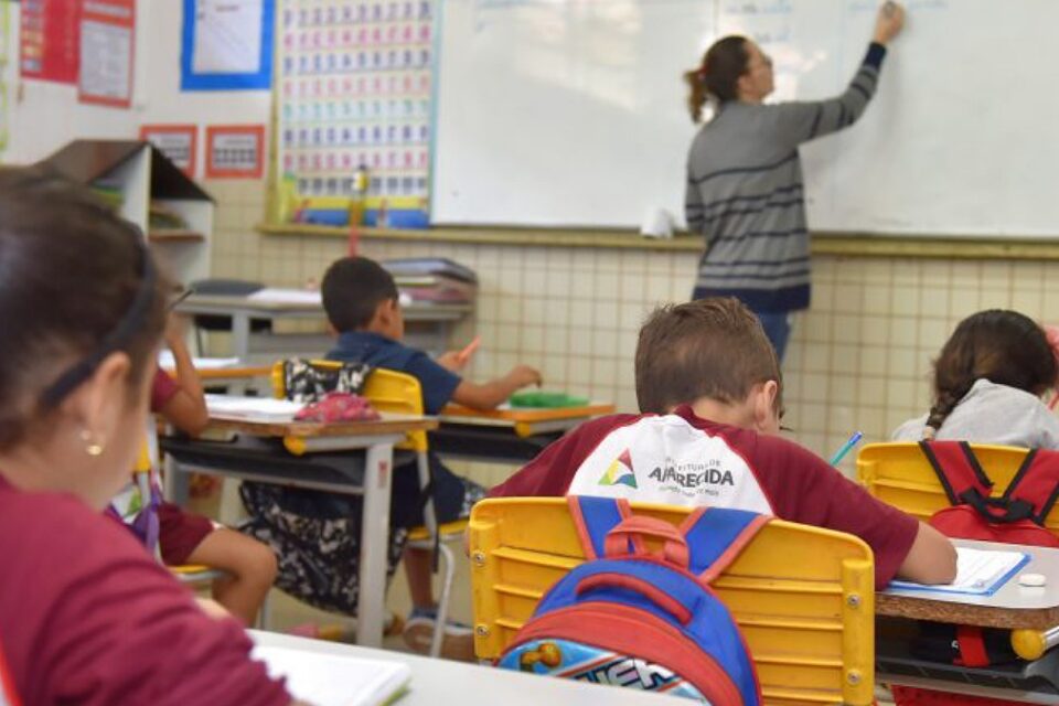 Sala de aula de AParecida de Goiãnia com alunos nas carteiras e professora escrevendo na lousa