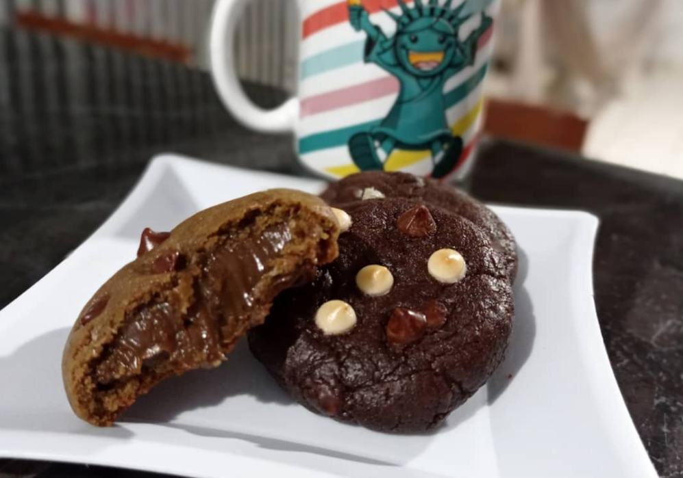 sabor de chocolate com recheio cortado ao meio, posicionado ao lado de outros dois de chocolate inteiros. A casa representa opção para comprar cookies em Goiânia
