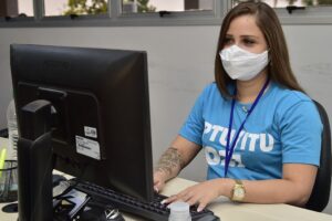 Atendente com camiseta IPTU e ITUno computador - Refis 2021: Prefeitura de Aparecida de Goiânia oferece até 90% de descontos em juros e multas