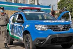 Dois policiais em frente a uma viatura da Polícia Militar
