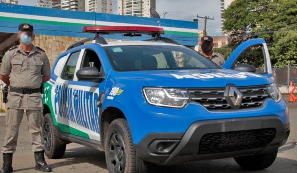 Dois policiais em frente a uma viatura da Polícia Militar