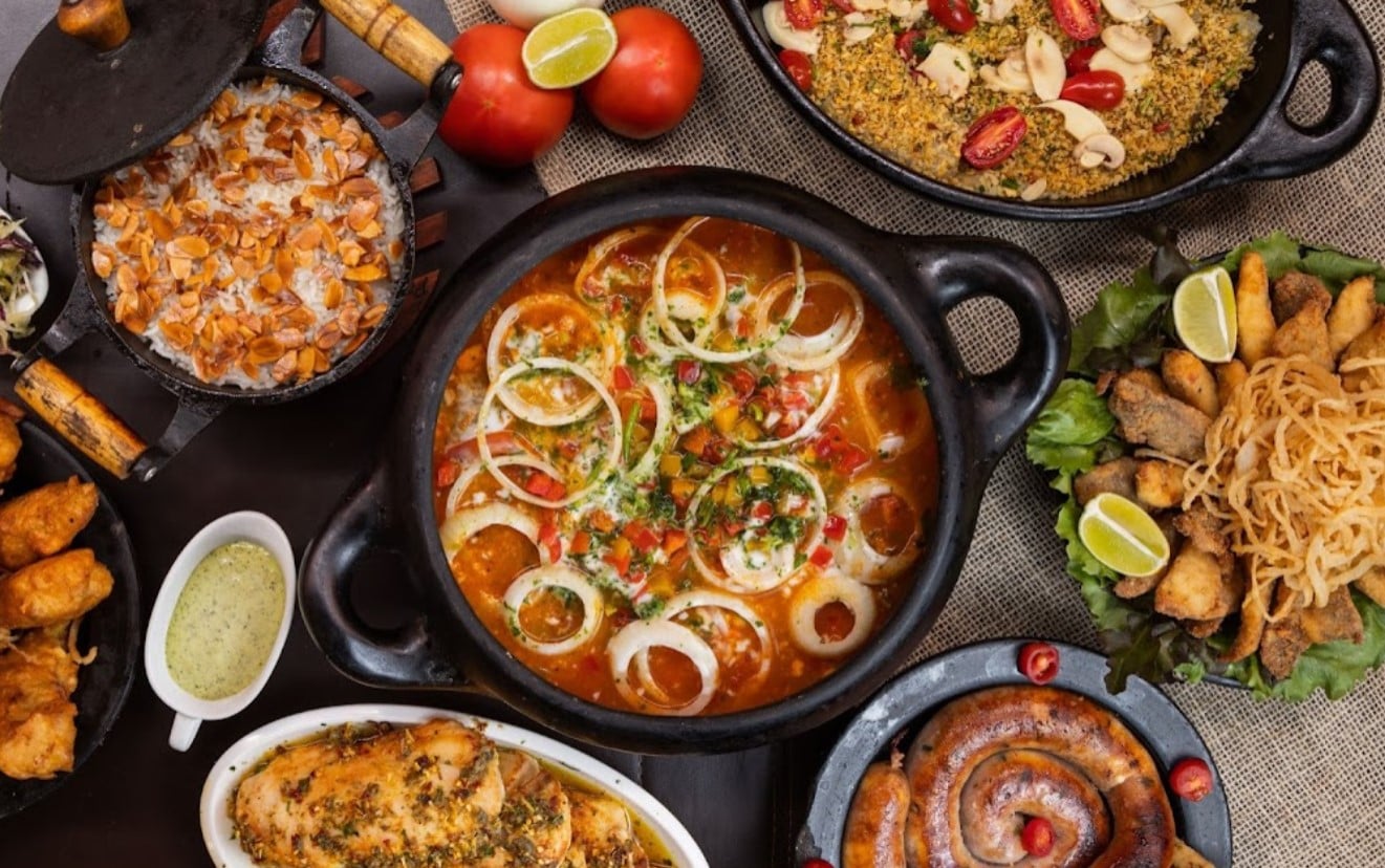 mesa com moqueca de peixe na panela de barro, farofa e acompanhamentos servidos ao lado, preparados pelo Armazém do Peixe, opção para comer peixes em Goiânia 