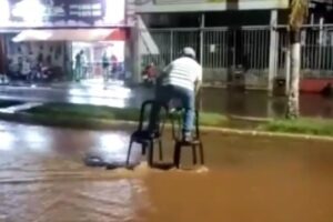 Um homem residente em Palmeiras de Goiás usou duas cadeiras de plástico para conseguir atravessar uma enxurrada na cidade. (Foto: reprodução)
