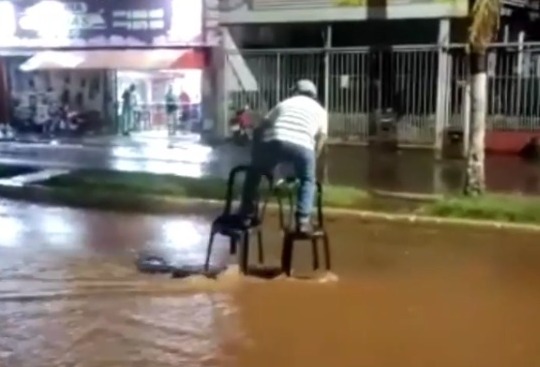 Um homem residente em Palmeiras de Goiás usou duas cadeiras de plástico para conseguir atravessar uma enxurrada na cidade. (Foto: reprodução)