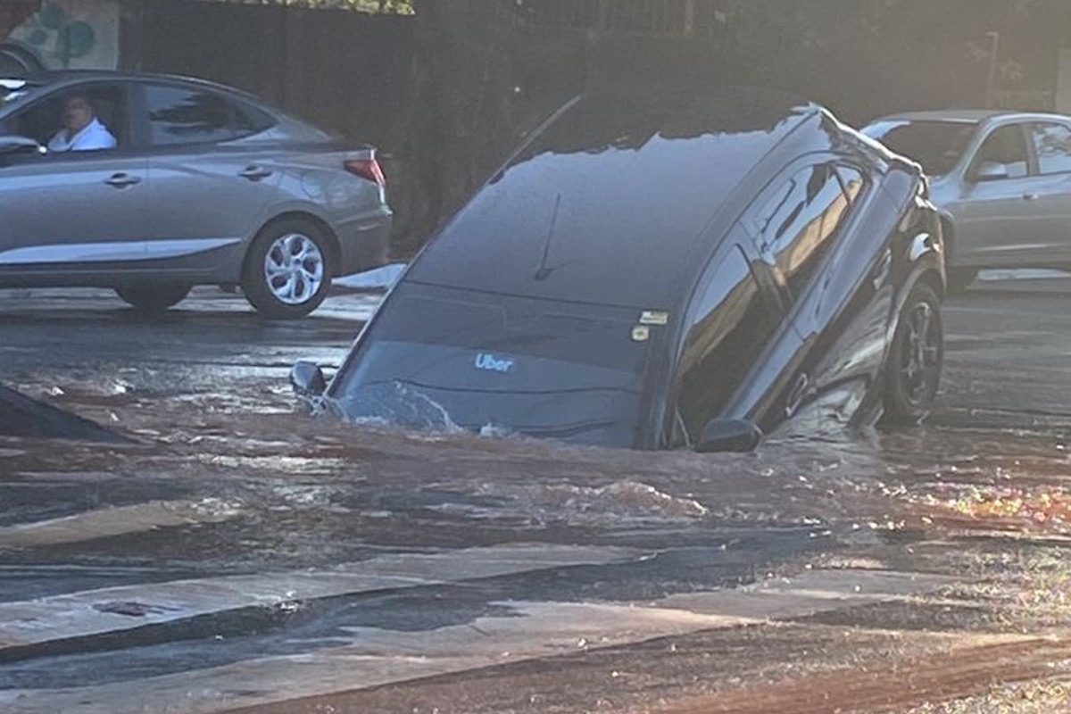 Um carro de passeio caiu em uma cratera que se abriu na Avenida Independência após uma adutora de água se romper, em Goiânia. (Foto: reprodução)