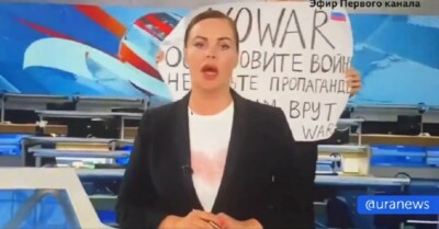 Marina Ovsyannikova, ao fundo, carrega cartaz contra a guerra na Ucrânia