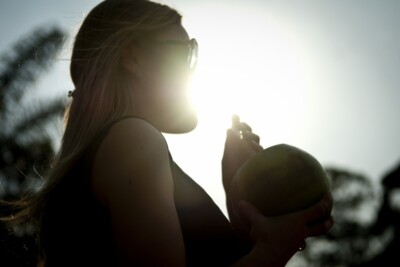 Imagem mostrar uma mulher se refrescando bebendo uma agua de coco