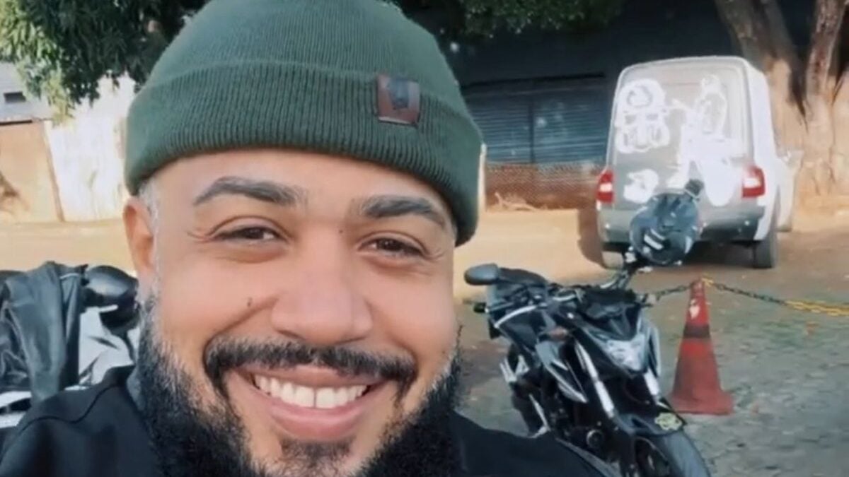 Imagem mostra Tourão sorrindo na frente de uma moto.