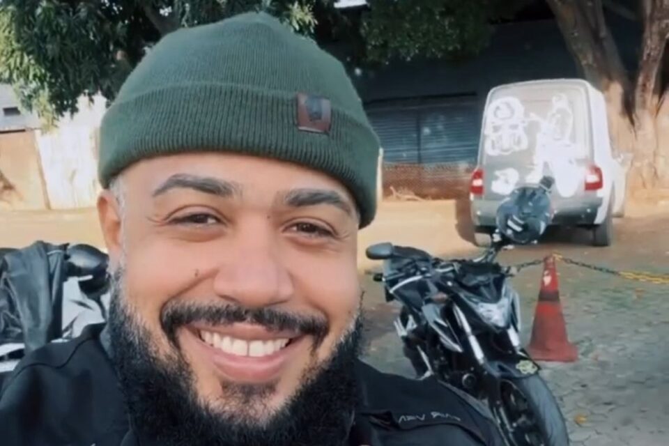 Imagem mostra Tourão sorrindo na frente de uma moto.