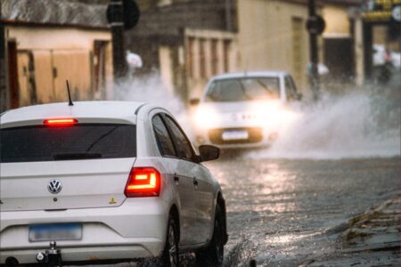 Imagem mostra dois carros passando em rua alagada após forte chuva em Goiás.