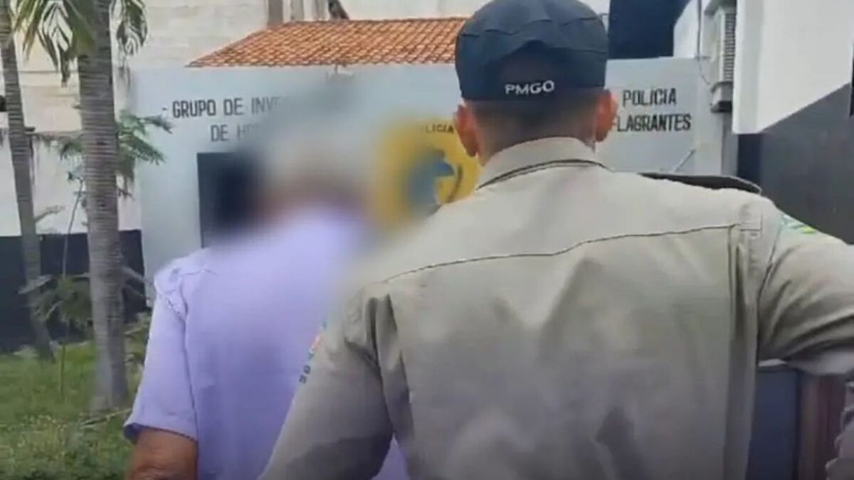 Dono de mercearia suspeito de estupro contra adolescente em Caldas Novas é conduzido para a delegacia por um policial militar.