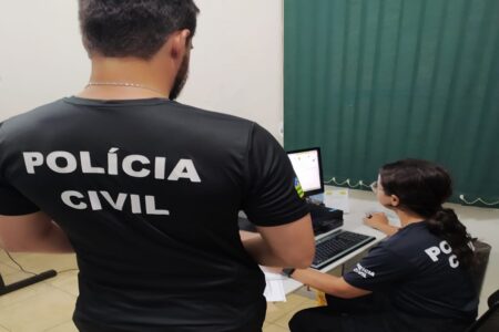 Imagem mostra agentes da polícia civil verificando um computador durante operação contra pornografia infantil em Goiás.