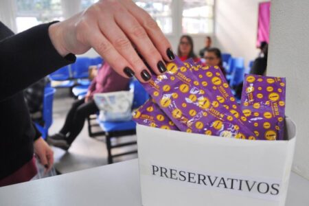 Mão feminina com esmaltes pretos pega camisinha gratuita em unidade de saúde Mulher pega camisinhas gratuitas em unidade de saúde (Foto: reprodução/Portal Arauto)