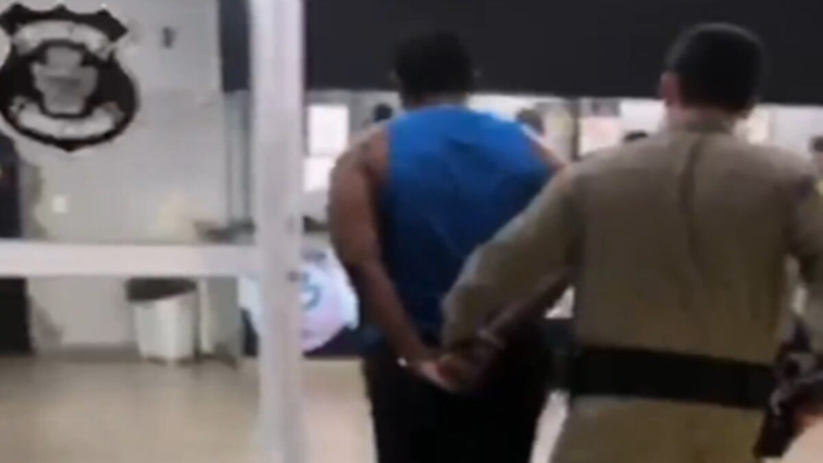 Imagem mostra suspeito de aplicar o golpe do aluguel em Goiânia sendo levado algemado para a delegacia.