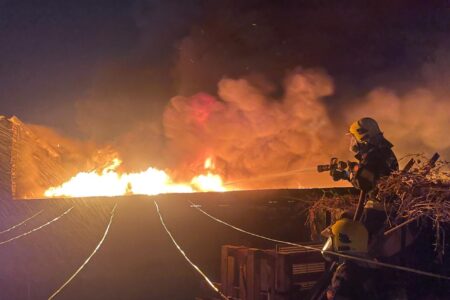 Foto colorida mostra bombeiro direcionando jato de água para foco de chama intenso (Foto: Bombeiros)