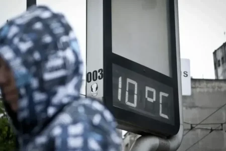 Imagem mostra uma pessoa de costas usando uma blusa com capuz cinza e branca e um termômetro ao fundo marcando frio de 10 ºC.