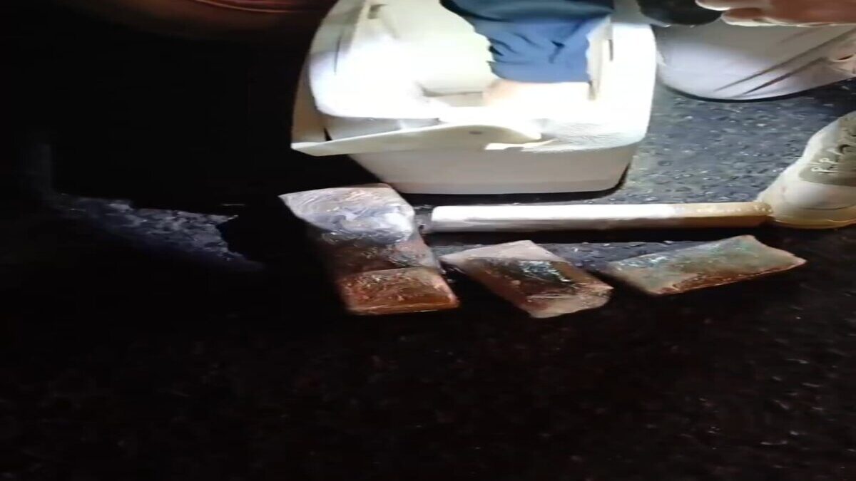 Imagem colorida mostra a mão de um policial segurando uma lanter e com a outra ele tira pacotes de drogas que estavam em uma caixa térmica.