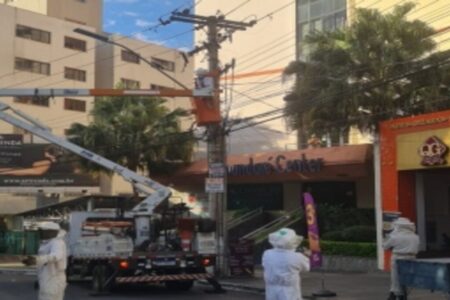 Imagem colorida mostra um caminhão guindaste levantado em frente a prédios