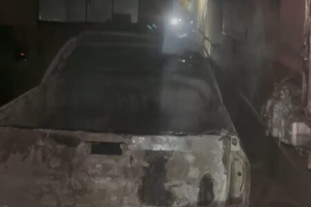 Imagem mostra um carro queimado na garagem de uma residência.