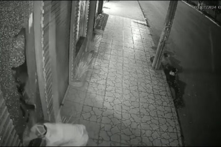 Imagem em preto e branco mostra um homem quebrando a porta de vidro de uma joalheria para invadir o local.
