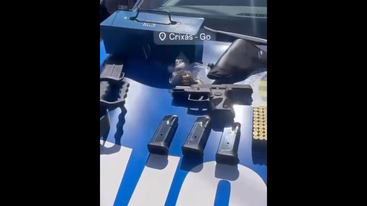 Imagem mostra armas, munições e uma mala azul de metal em cima do capô de uma viatura da Polícia Militar.