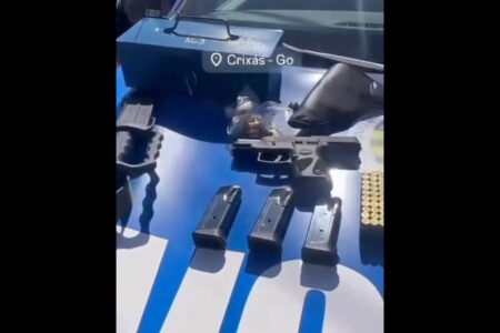 Imagem mostra armas, munições e uma mala azul de metal em cima do capô de uma viatura da Polícia Militar.