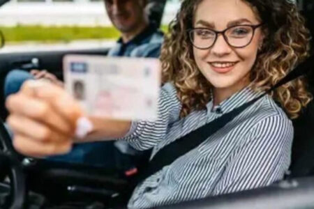 Imagem colorida mostra uma mulher dentro de um carro, usando cinto de segurança e segurando uma Carteira Ncional de Habilitação.