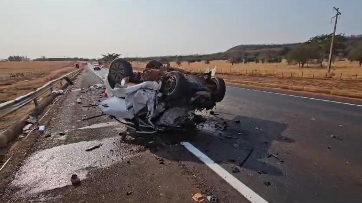 Imagem colorida mostra um carro branco destruído após um acidente em uma rodovia.