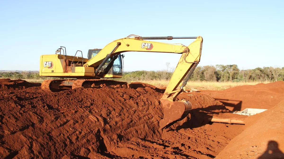 Imagem colorida mostra uma máquina retroescavadeira em um terreno de terra
