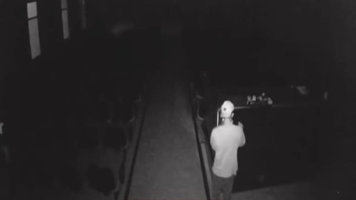 Imagem em preto e branco mostra um homem dentro de uma igreja. Ele usa uma camiseta e um boné branco